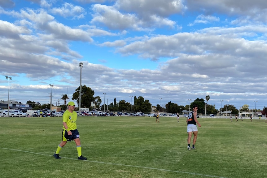 A boundary umpire and a player near the boundary line during a country football game.