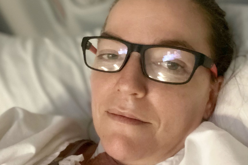 Woman with hair pulled back, glasses, laying in hospital bed.