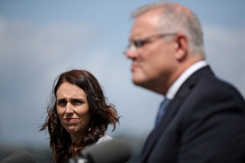 Jacinda Ardern squints while looking into the sun, Scott Morrison is visible out of focus in foreground