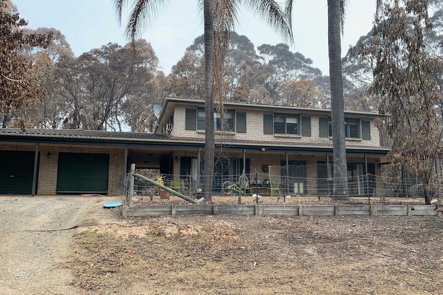 A house in the bush surrounded by burnt trees.