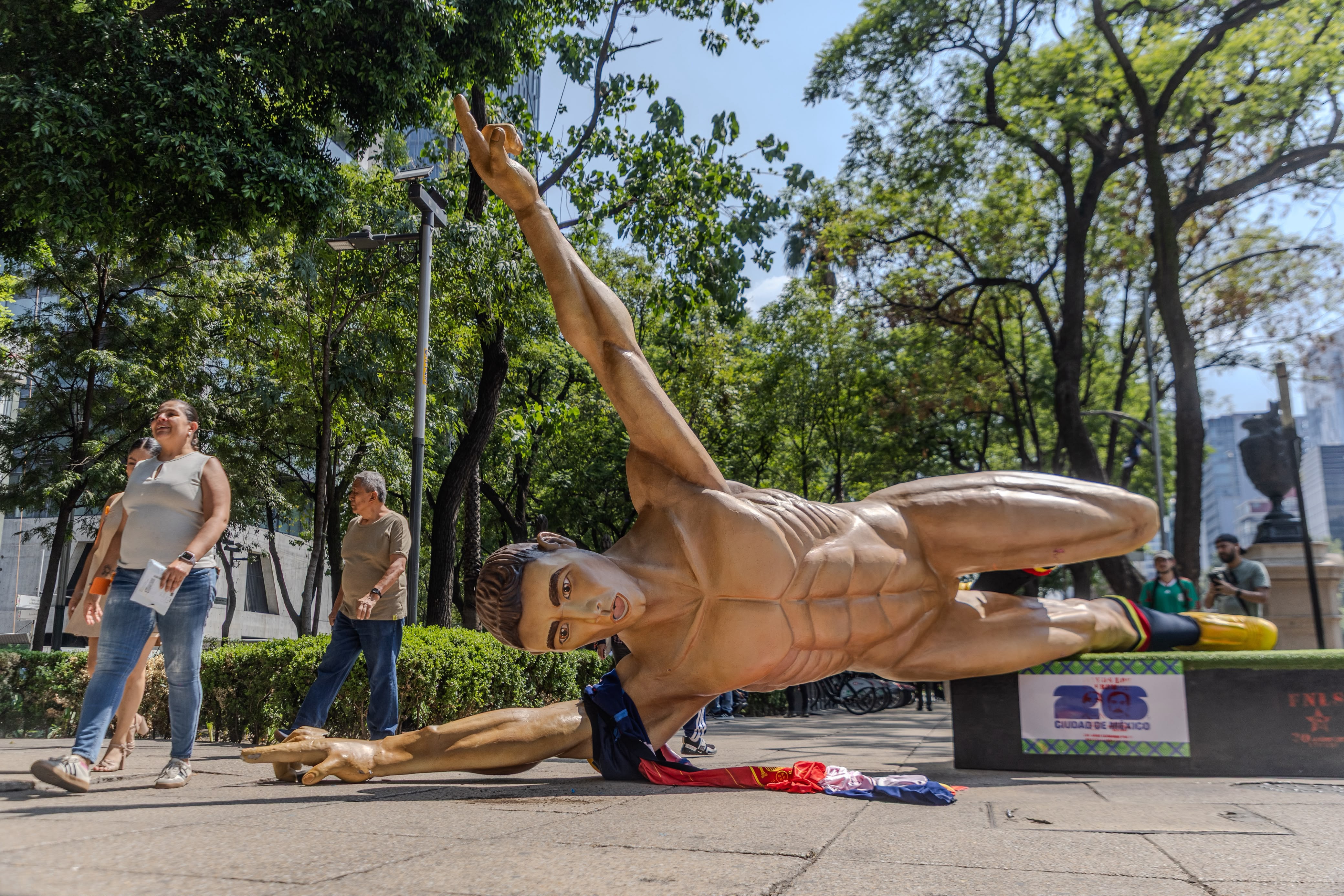 A giant statue of a naked male footballer is lying on its side after being torn down