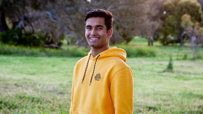 A young man in a yellow jumper smiles at the camera