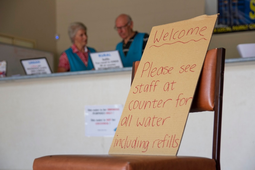 Sign on chair and two staff at warehouse where supplies of donated drinking water are distributed.