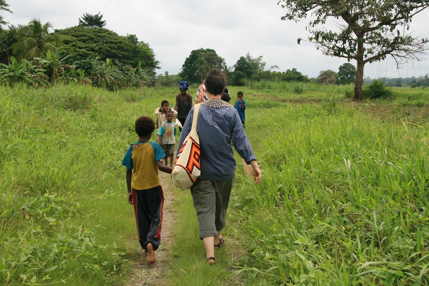 A woman and child walk hand-in-hand along a track towards a group of people in rural Papua New Guinea.