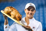 Ash Barty smiles as she holds up a trophy featuring a model of a wombat.