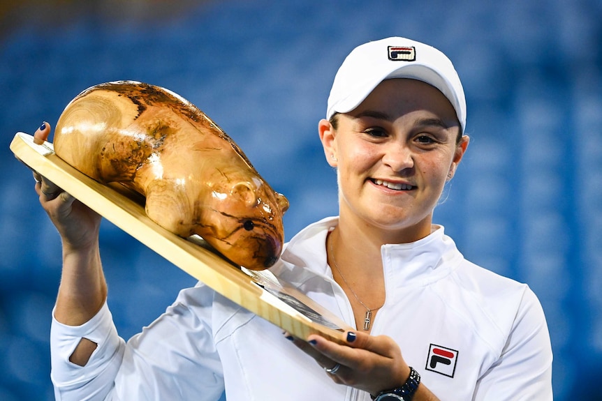 Ash Barty smiles as she holds up a trophy featuring a model of a wombat.