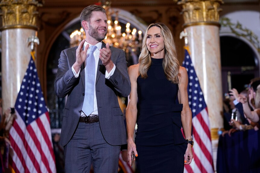Eric and Lara Trump stand on stage surrounded by United States flags.