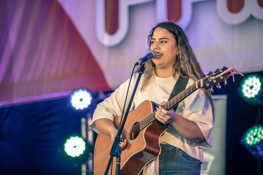 A young performer singing and playing guitar on a stage in central tamworth