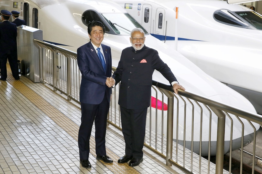 Shinzo Abe and Narenda Modi stand in front of a Shinkasen bullet train.