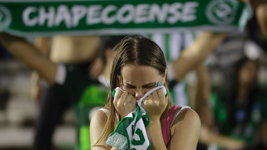 A fan of Brazil's soccer team Chapecoense crying into her scarf, another scarf in the background.