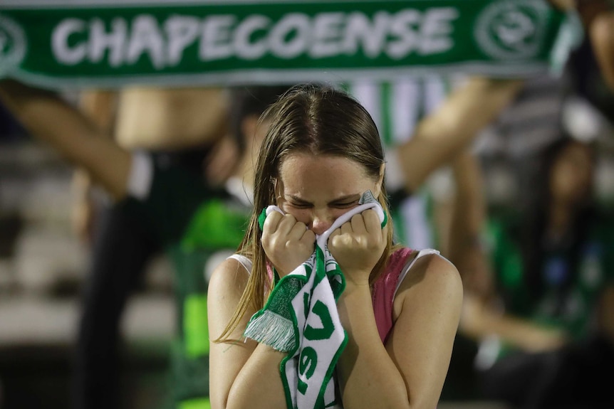 A fan of Brazil's soccer team Chapecoense crying into her scarf, another scarf in the background.