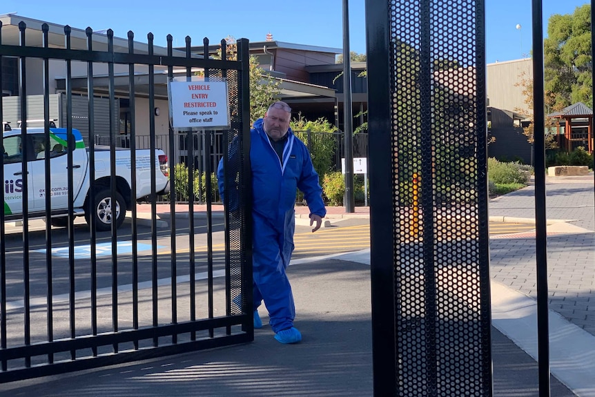 A man wearing a blue protective suit shutting a gate at Pennington school