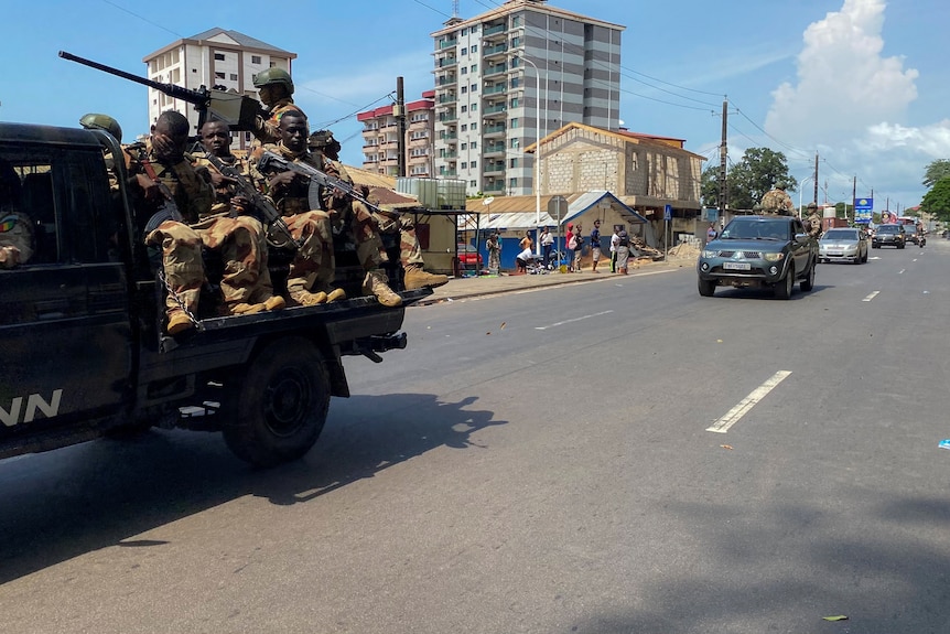 A truck carring armed African soldiers travels down a city street.