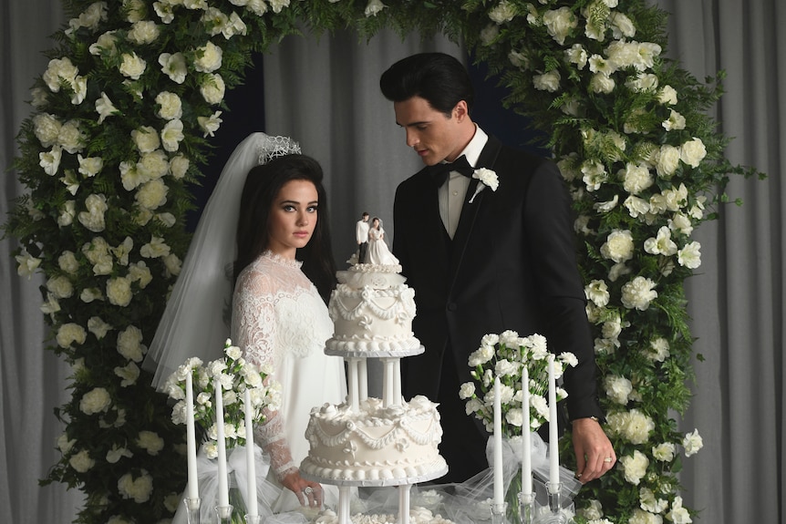 Cailee Spaeny and Jacob Elordi in character as Priscilla and Elvis Presley in front of their wedding cake