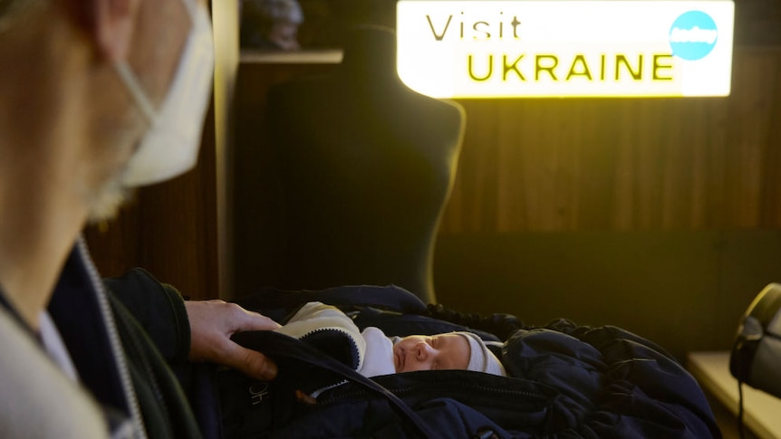 baby in carrier in front of sign reading "visit ukraine"