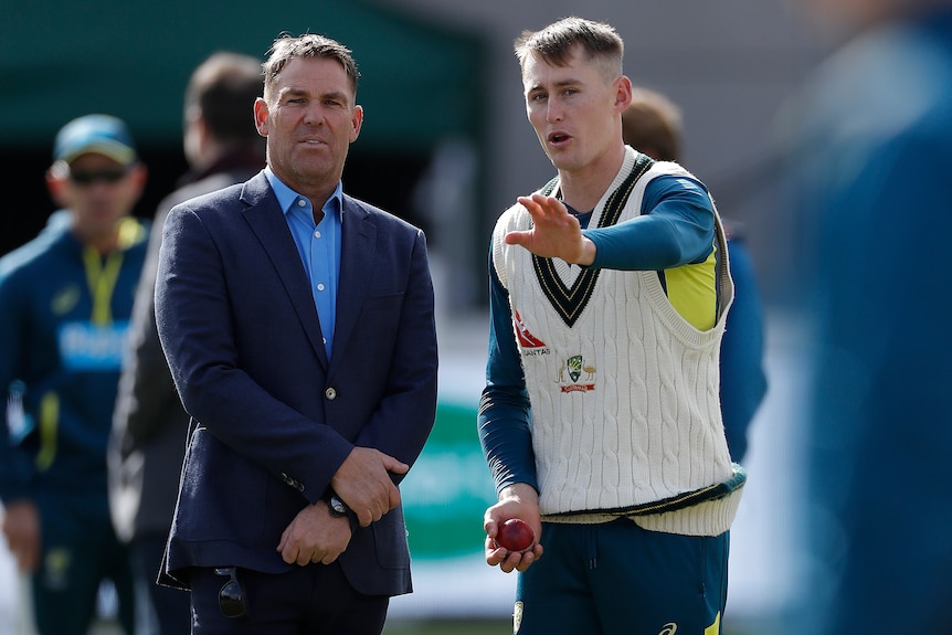 A former cricket player in a suit offers advice to a current player during a warm up