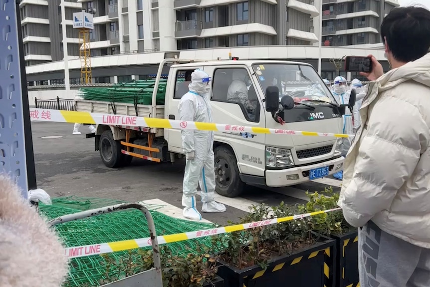 穿防护服的警察站在绿色的金属隔离栏外