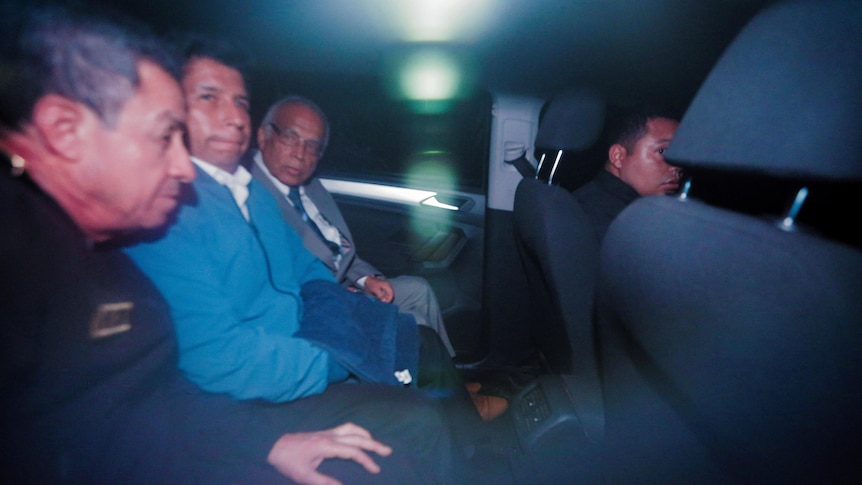 Outsted Peruvian president Pedro Castillo sits in the middle seat between two others in the back of a car.