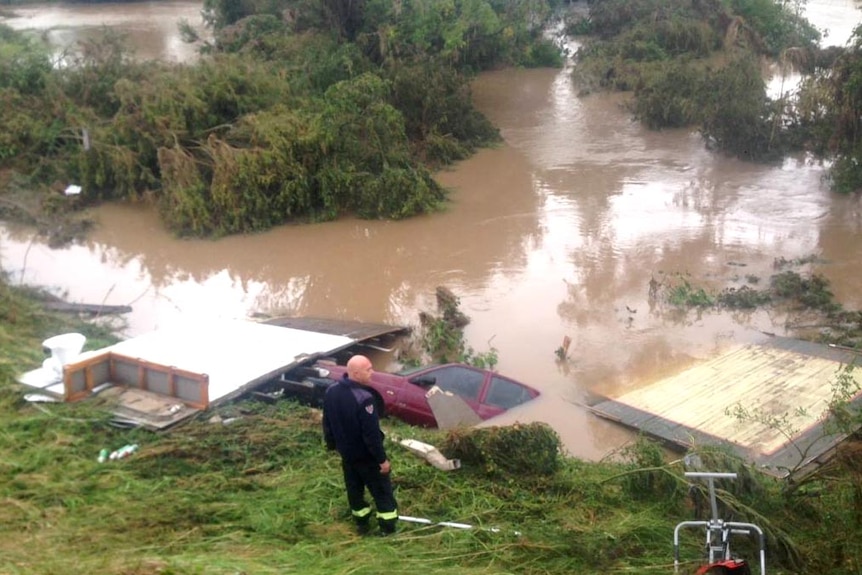 A fire officer stands next to a submerged car, surrounded by debris from the Dungog floods.