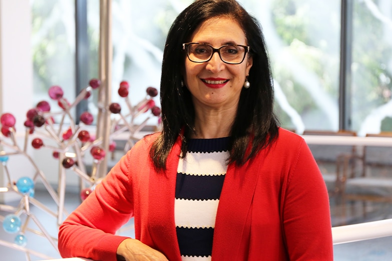 A woman with glasses stands smiling in a well lit room.