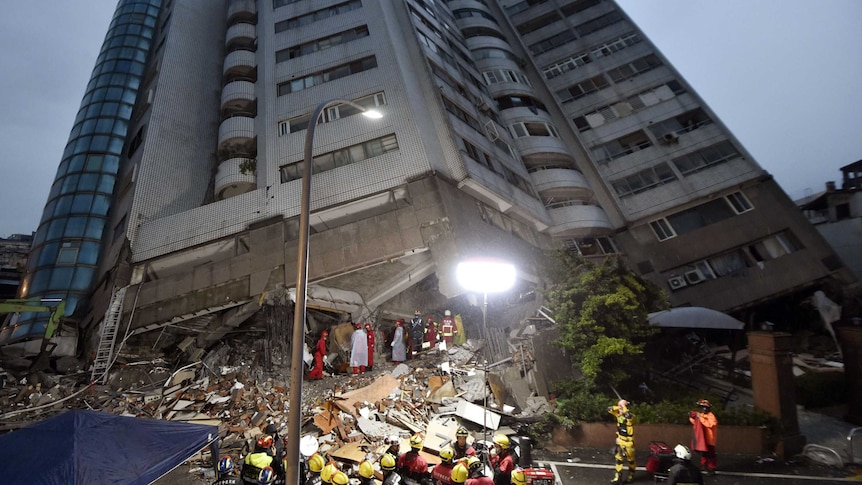 Rescue workers work on the site of a leaning apartment building.