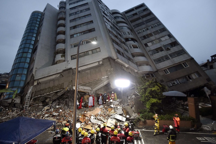 Rescue workers work on the site of a leaning apartment building.