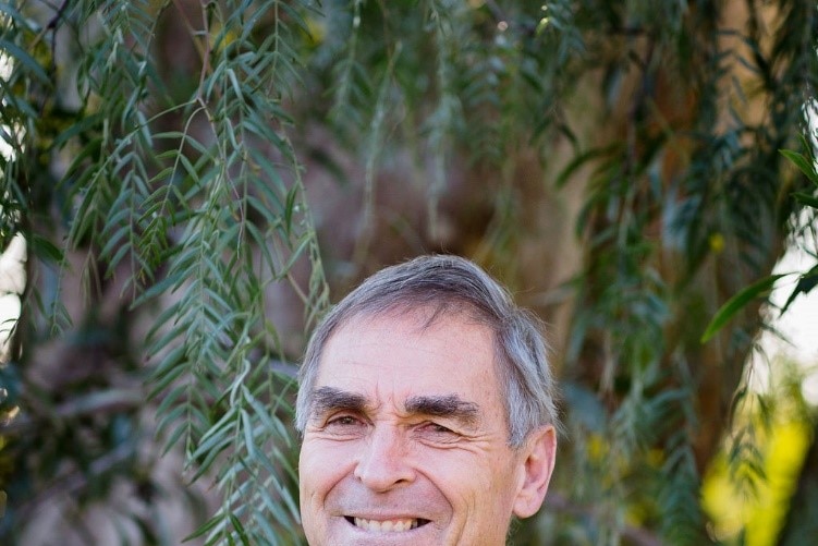 A man with greying hair stands smiling at the camera.