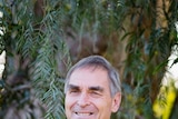 A man with greying hair stands smiling at the camera.
