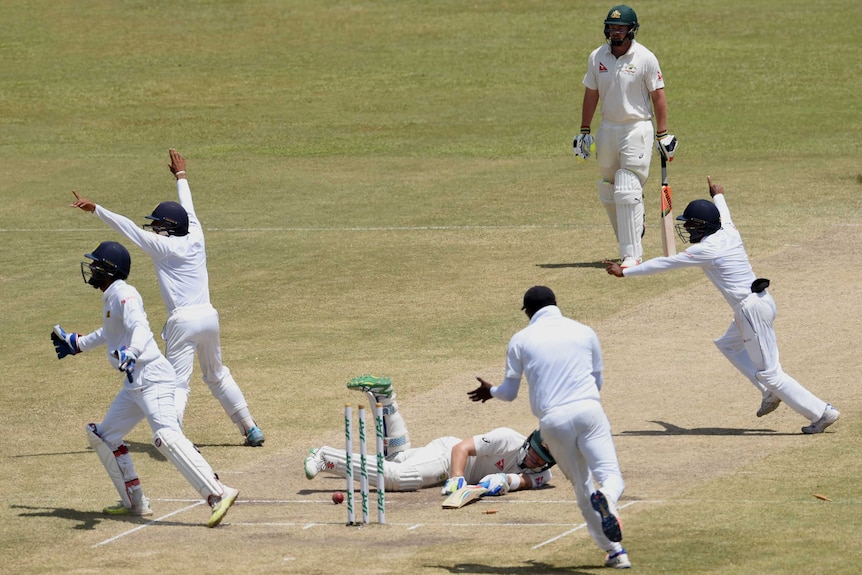 Sri Lanka cricket teammates celebrating on the field while Australia batsman Peter Nevill lies on the ground in defeat.