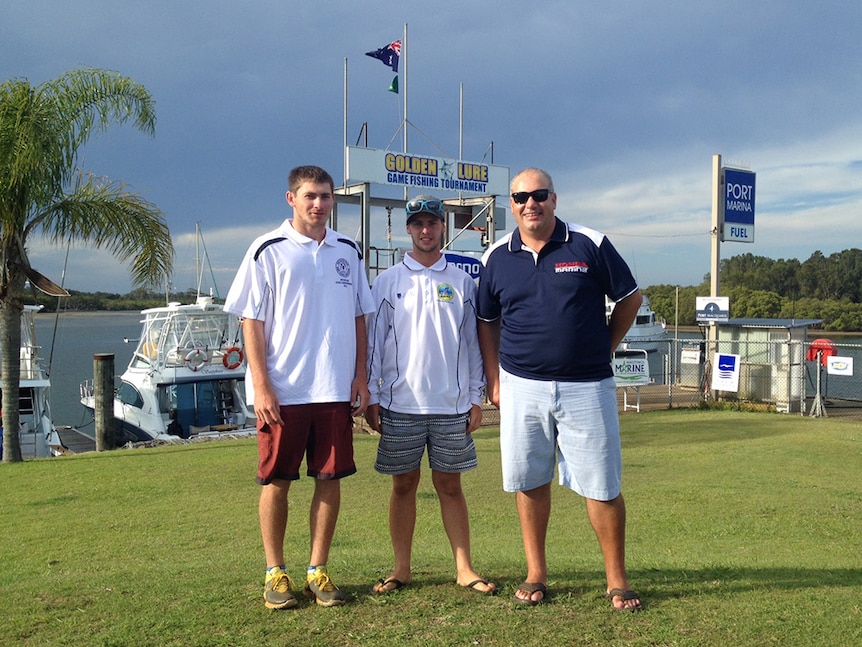 Three game fishermen stand on a hill behind the Golden Lure signage at the marina in Port Macquarie.