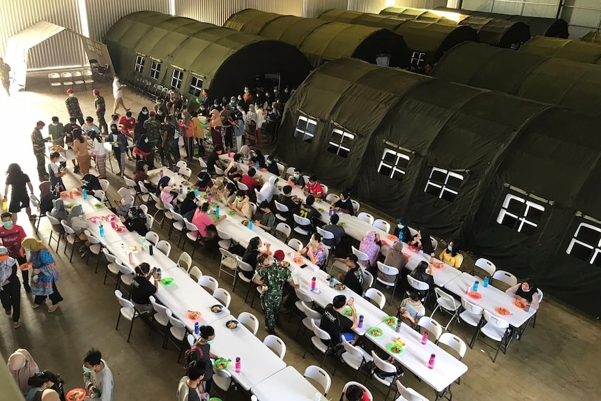 A military hangar with long white tables and green army tents.