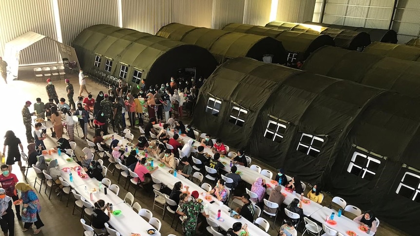 A military hangar with long white tables and green army tents.