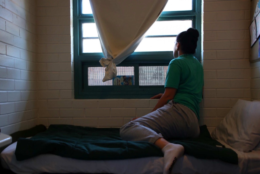 Prisoner Sam sits on her cell bed and looks out of the window.