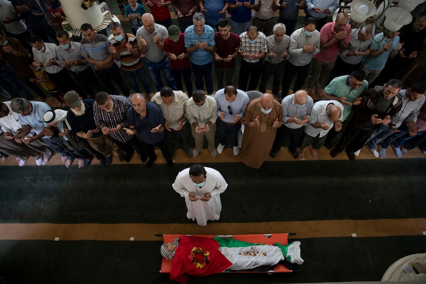 Palestinian mourners pray in rows by the body of a woman wrapped in a Palestinian flag.