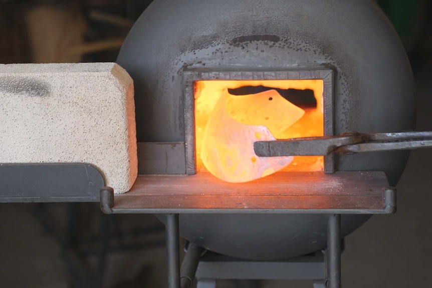 A piece of metal being pulled out of a red hot fire with thongs