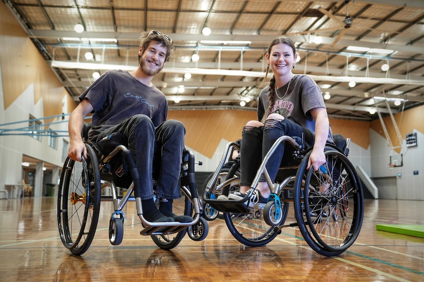 A young man and woman sit in wheelchairs smiling broadly.