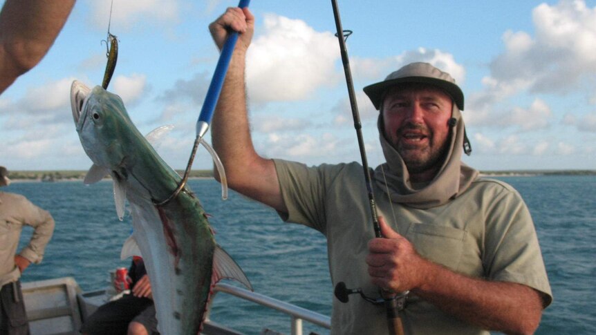 Dr Tim Stone holds up a fish he's caught on a boat.