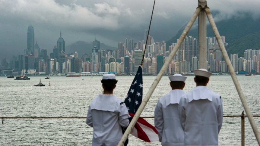 Three US Navy soldiers in white are seen out of focus onboard a ship as they look across the harbour to Hong Kong's skyscrapers.