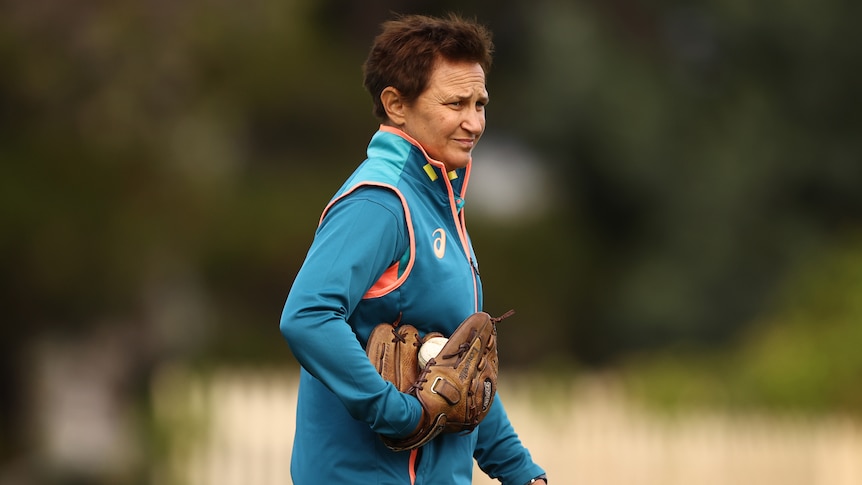 Australian women's cricket coach is seen before a game holding one cricket ball in her hand and another in a baseball glove.