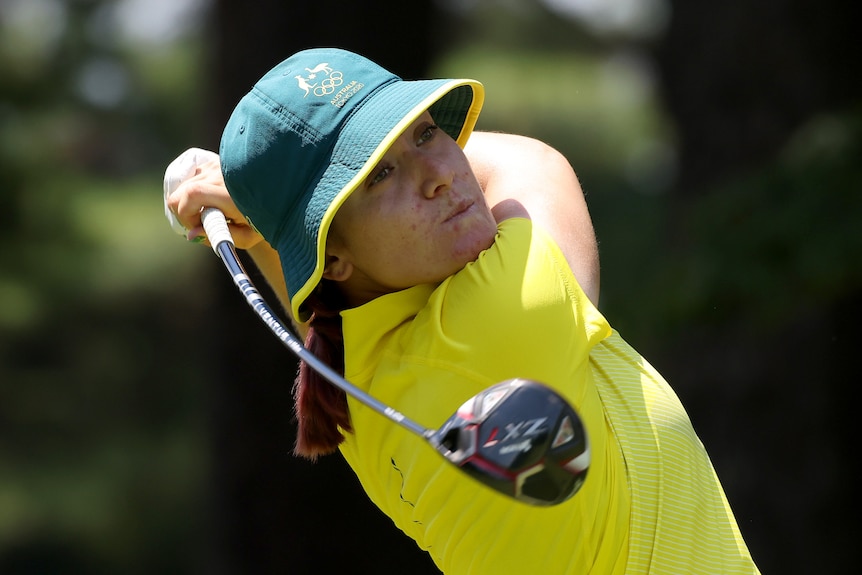 Hannah Green, wearing a green bucket hat and gold shirt, swings her golf club behind her head