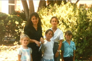 Judith Fordham outside in front of green bushes with four children standing in front of her.