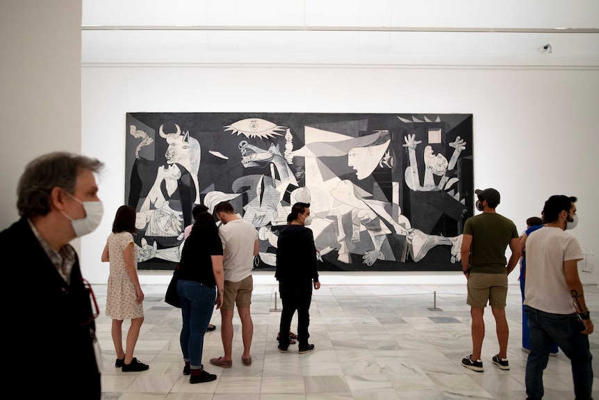 People wearing face masks stand in front of black and white painting in a museum.