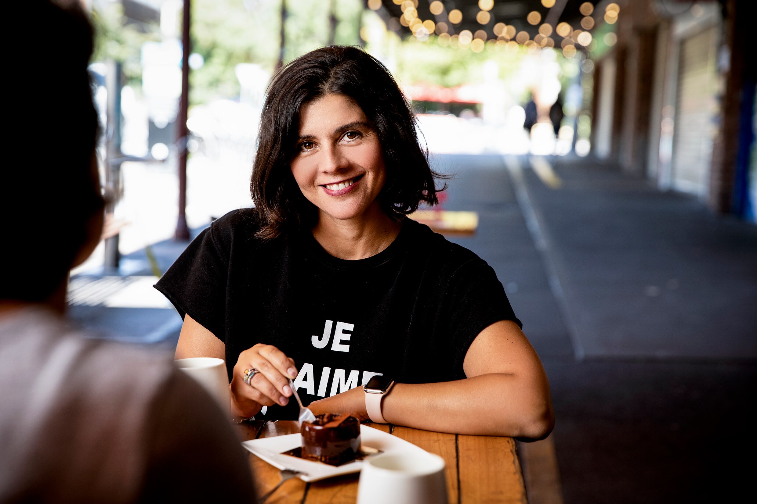 A smiling woman with brown hair sits at a cafe