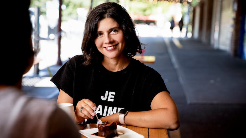 A smiling woman with brown hair sits at a cafe