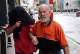 Carl Allan Bridge, wearing a jacket over his head, is guided away from court by an unidentified man.