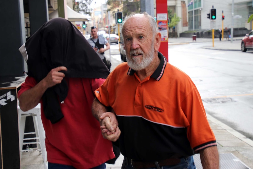 Carl Allan Bridge, wearing a jacket over his head, is guided away from court by an unidentified man.