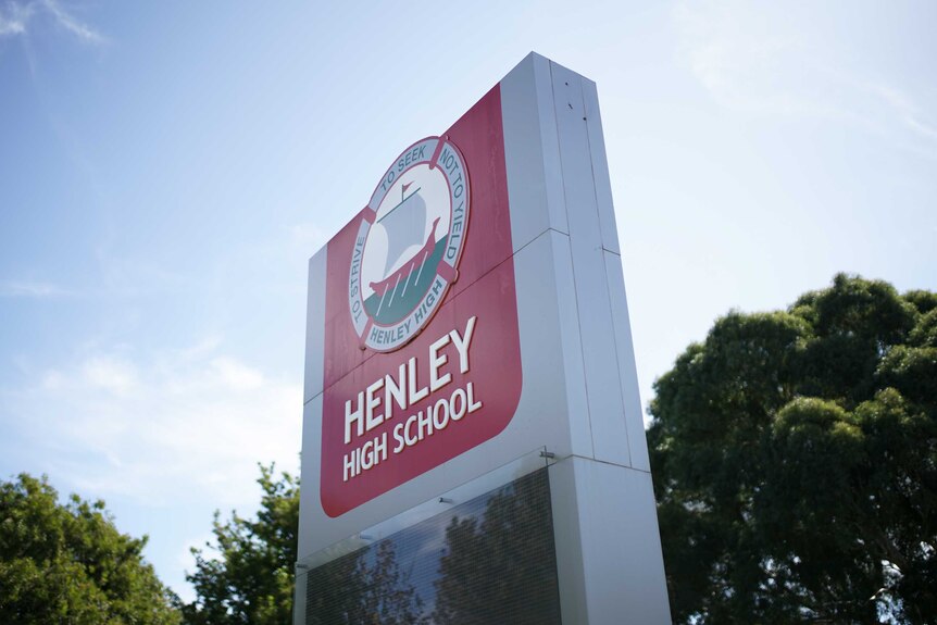 A sign outside in front of trees with the words "Henley High School" on it