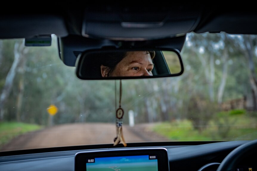 Heidi is seen in the rear view mirror as she drives along a tree-lined, rural road.