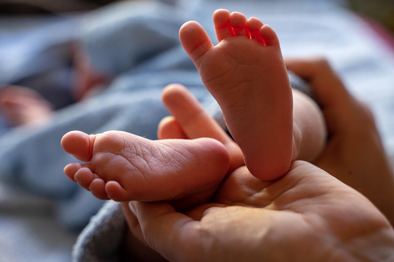 An adults holds a baby's feet in the palm of their hands.