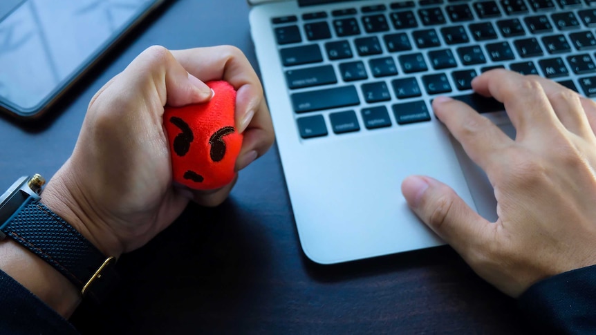 Cropped hand of businessman pressing stress ball while using laptop
